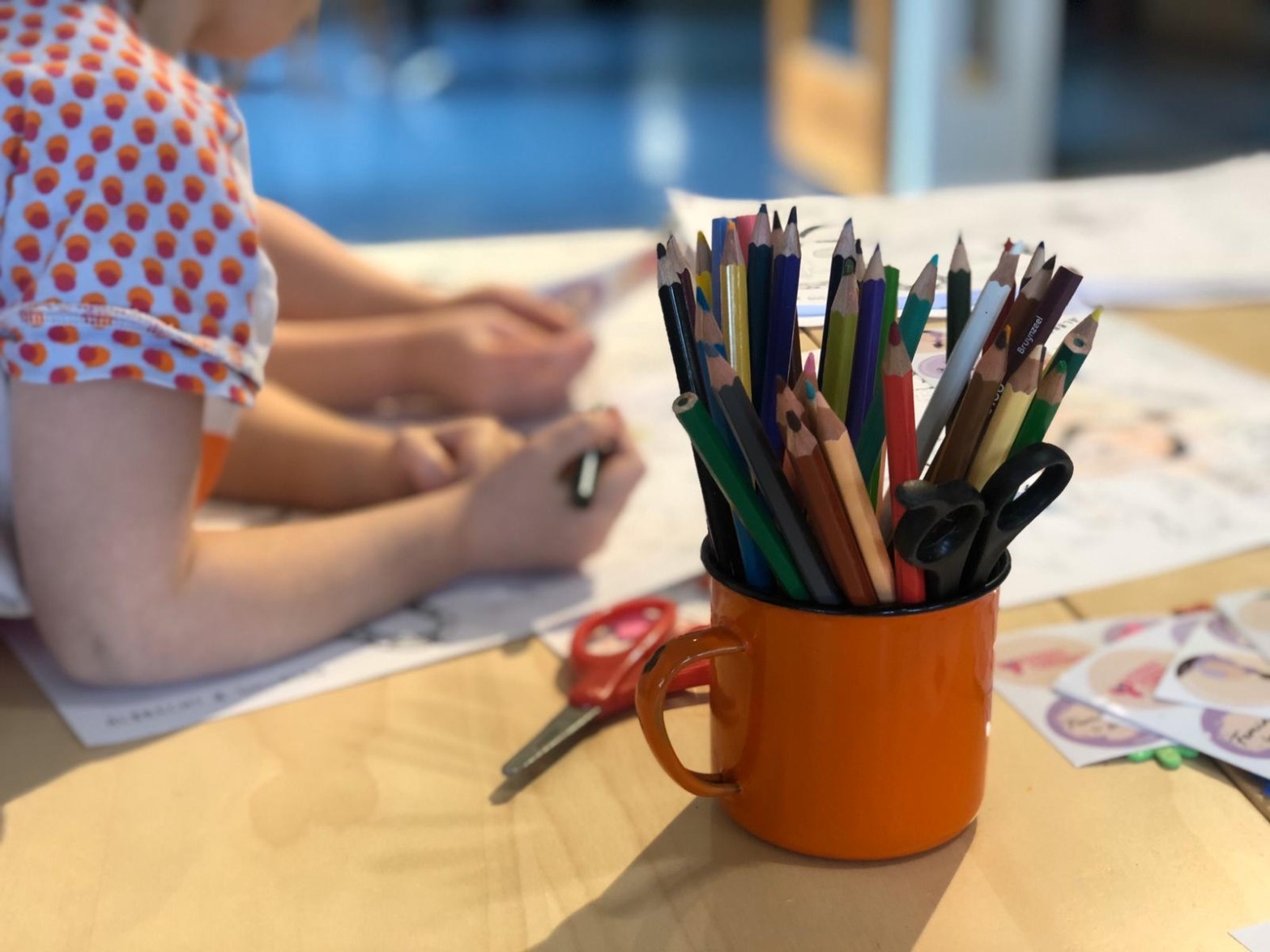 Kopp med pennor och två barn som färglägger i bagkrunden