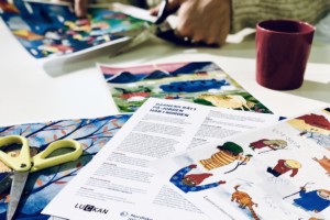 Pedagogiskt material strödda ut på ett bord med någon som klipper ett papper i bakgrunden