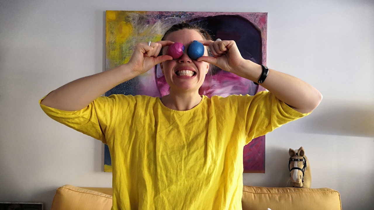 Linda håller upp två jongleringsbollar framför ögonen och ler brett