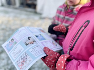 Två barn är utomhus i vinterkläder och tittar in i vinterboken